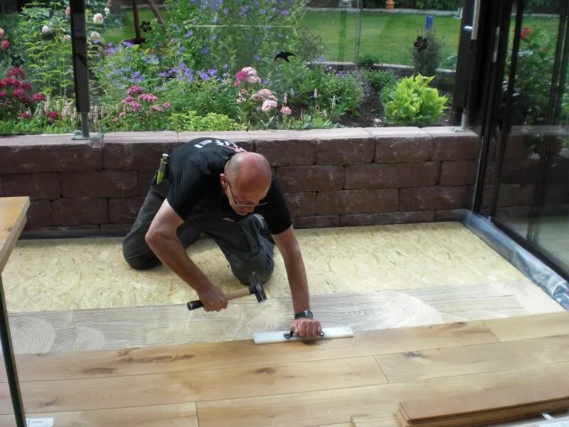 Bernd Teufel verklebt Holzdielen in einem Wintergarten